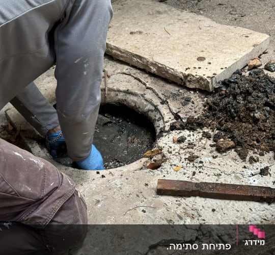 אדם עם כפפות כחולות עובד על פתח ביוב
